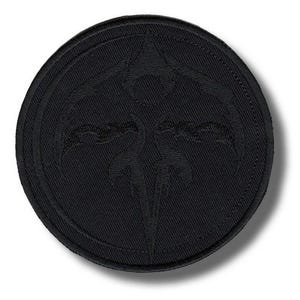 Könnte beinhalten: Ein runder, schwarz gestickter Aufnäher mit einem stilisierten Emblem innerhalb eines kreisförmigen Rahmens. Das Emblem hat ein zentrales, vertikales Element mit geschwungenen, flügelartigen Formen. Der Aufnäher besteht aus einem strukturierten Stoff.