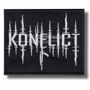 May include: Black rectangular patch with the word "KONFLICT" embroidered in white, stylized with vertical and horizontal lines. The patch has a black border and a shadow effect.