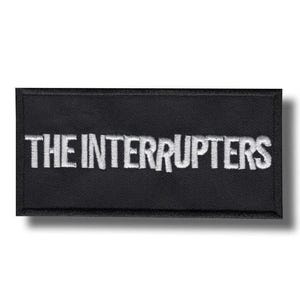 Op de afbeelding: Zwart rechthoekig embleem met de geborduurde tekst "THE INTERRUPTERS" in het wit. Het embleem heeft een eenvoudig, strak ontwerp, geschikt voor toepassing op kleding of accessoires. De tekst is in een vetgedrukte, schreefloze lettertype.