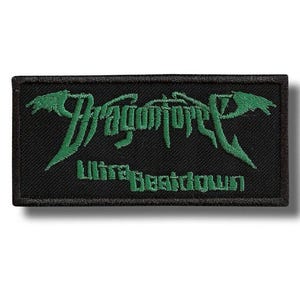 Pode incluir: Patch retangular preto com texto bordado em verde. O texto diz "Dragonforce" em uma fonte estilizada acima de "Ultra Beatdown". O patch tem uma borda preta e é provavelmente para roupas ou acessórios.