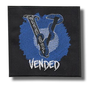 May include: Square black patch with a blue and white embroidered design. The design features a stylized letter "V" with a snake-like element, set against a blue background. The word "VENDED" is embroidered in white below the design.