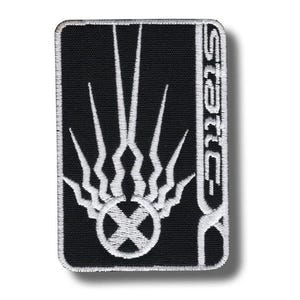 May include: Black rectangular patch with white embroidered design. The design features a stylized flame or sunburst above a circle with an X inside. The word "STATIC" is vertically embroidered on the right side.