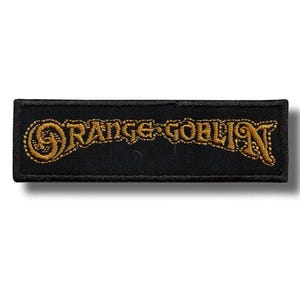 May include: Black rectangular patch with the embroidered text "ORANGE GOBLIN" in gold. The patch has a decorative border and is likely for a jacket or bag.