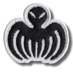 May include: Embroidered patch featuring a black alien-like figure with white accents and a white border. The design includes a head with two white eye shapes and a body with curved lines, resembling wings or arms.