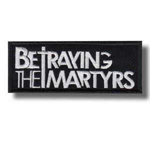 Könnte beinhalten: Ein rechteckiger, schwarzer, gestickter Aufnäher mit den weißen Worten "BETRAYING THE MARTYRS". Der Aufnäher hat einen schwarzen Rand und ist zum Aufnähen auf Kleidung oder Accessoires gedacht.