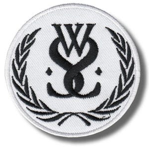 May include: A round, white embroidered patch with a black design. The design features intertwined letters "W" and "S" in the center, surrounded by a laurel wreath. The patch has a stitched border.