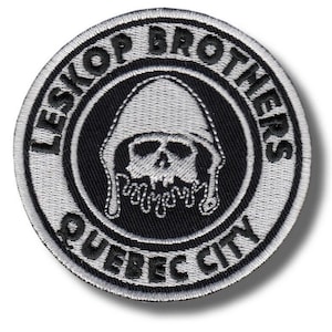 Pode incluir: Um patch circular com o texto "LESKOP BROTHERS QUEBEC CITY" em branco. O patch apresenta um design central de uma caveira usando um capacete, com detalhes gotejantes, tudo em preto e branco.