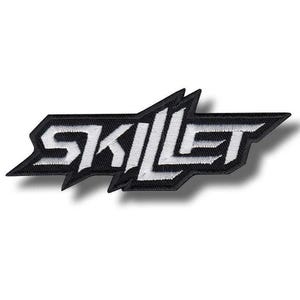 May include: Black and white embroidered patch featuring the word "SKILLET" in a stylized, angular font. The patch has a black background with white lettering and a unique, jagged border design. Ideal for jackets, bags, or other fabric items.