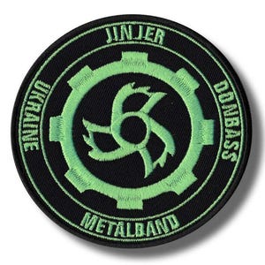 May include: A round black patch with green embroidered text and design. The text reads "JINJER", "UKRAINE", "DONBASS", and "METALBAND". The central design is a stylized green gear.