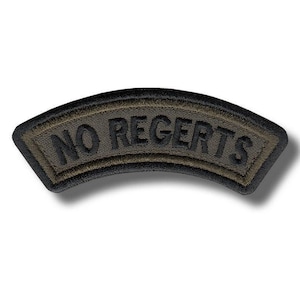 May include: A curved, embroidered patch with the words "NO REGRETS" in black lettering. The patch has a dark olive green background with a black border. The patch is likely designed to be sewn onto clothing or gear.