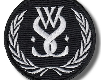 May include: A round, black embroidered patch featuring a white intertwined design of the letters "W" and "S" with a stylized laurel wreath border. The patch is circular and has a textured appearance.