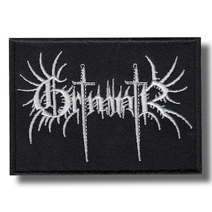 以下が含まれることがあります： 白の刺繍テキストと画像が施された黒い長方形のパッチ。テキストはバンド名で、2本の剣と翼のようなデザインが施されています。ジャケットやバッグ用です。