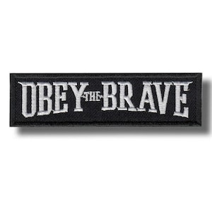 May include: A rectangular black patch featuring the embroidered words "OBEY THE BRAVE" in white, bold lettering. The patch has a black border and is designed to be sewn onto clothing or accessories.