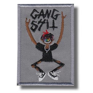 Può includere: Toppa ricamata con sfondo grigio e un personaggio dei cartoni animati con le braccia alzate. Il personaggio ha la pelle marrone, una maglietta nera e pantaloni strappati. Il testo "GANG 571" è sopra il personaggio.