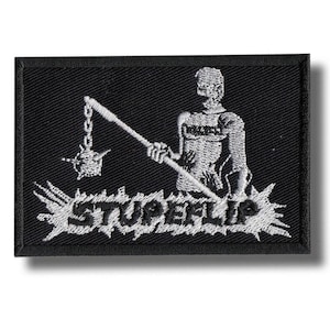 May include: Black rectangular patch with a white embroidered design. The design features a figure holding a flail, with the word "STUPEFLIP" in a stylized font below. The patch has a black border.