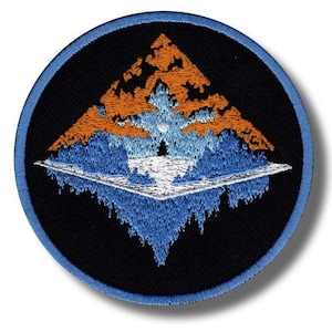 Könnte beinhalten: Gestickter Aufnäher mit einem Berglandschaftsdesign. Der Aufnäher hat einen schwarzen Hintergrund und einen blauen Rand. Der Berg ist orange und blau, mit einer weißen und blauen Reflexion darunter. In der Mitte befindet sich ein kleiner weißer Kreis.