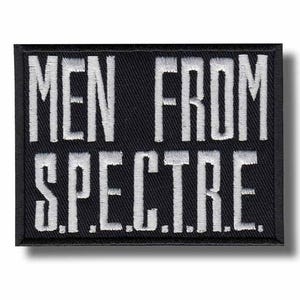 May include: A rectangular black patch with white embroidered text. The text reads "MEN FROM S.P.E.C.T.R.E." in a bold, sans-serif font. The patch has a black border and a shadow.