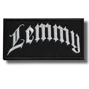 Pode incluir: Patch retangular preto com o nome "Lemmy" bordado em branco com letras góticas. O patch tem uma borda preta e provavelmente foi projetado para ser costurado em roupas ou acessórios.