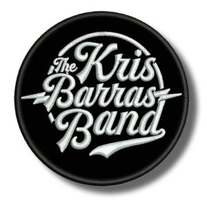 Puede incluir: Un parche circular negro con texto bordado en blanco. El texto dice "The Kris Barras Band" en una fuente estilizada. Diseños de rayos flanquean el nombre de la banda. El parche es probablemente para ropa o accesorios.