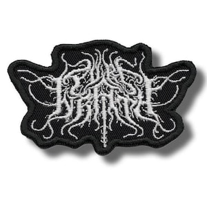 May include: Black embroidered patch with a white, stylized design and text. The patch has a black border and a unique, organic shape. The white design appears to be a complex, abstract pattern. This patch is suitable for jackets, bags, or other fabric items.