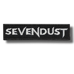 Puede incluir: Parche rectangular negro con el texto blanco bordado "SEVENDUST". El parche tiene un borde negro y probablemente está hecho de tela. El texto está en una fuente audaz y estilizada.