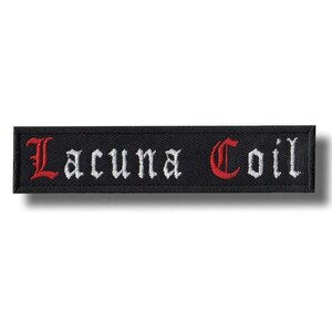 Puede incluir: Parche rectangular negro con las palabras "Lacuna Coil" bordadas en letras góticas blancas y rojas. El parche tiene un borde negro y probablemente está hecho de tela.