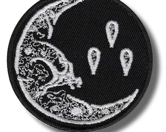 May include: Round black patch with a crescent moon design. The moon is white with intricate detailing, and three white teardrop shapes are below it. The patch has a black border and is likely an iron-on or sew-on patch.