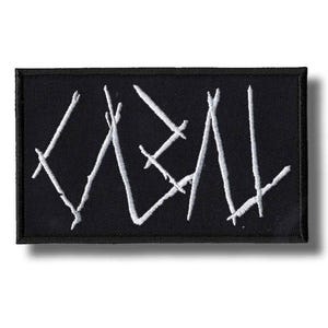 Puede incluir: Parche rectangular negro con la palabra "KVEN" bordada en blanco con una fuente estilizada y angular. El parche tiene un borde negro y está diseñado para coser o planchar sobre tela.