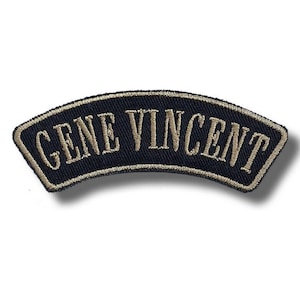 Op de afbeelding: Een marineblauwe geborduurde patch met de tekst "GENE VINCENT" in beige letters. De patch heeft een gebogen, gewelfde vorm met een beige rand. De patch is waarschijnlijk bedoeld voor kleding of accessoires.