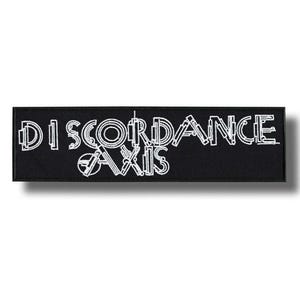 Puede incluir: Parche rectangular negro con las palabras blancas "DISCORDANCE AXIS" en letras de bloque estilizadas. El parche es probablemente de tela y tiene un borde blanco. El texto está centrado en el parche.