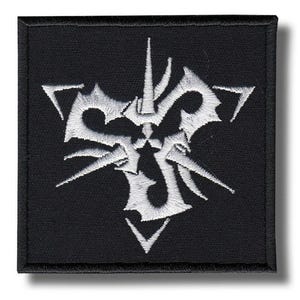 Op de afbeelding: Vierkante zwarte patch met een wit, gestileerd embleem. Het embleem heeft een centraal ontwerp met scherpe, hoekige elementen en een symmetrische indeling. De patch is bedoeld voor kleding of accessoires.