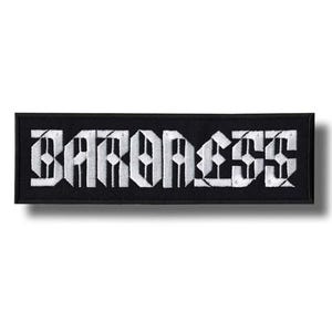 Op de afbeelding: Zwart rechthoekig embleem met het woord "BARONESS" geborduurd in witte gotische letters. De patch is een rechthoek met afgeronde hoeken en een zwarte rand. De tekst is gecentreerd en in een vetgedrukte, gestileerde lettertype.