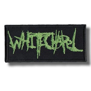 Peut inclure: Écusson rectangulaire noir avec le mot "WHITECHAPEL" brodé en vert, avec des lettres stylisées et dentelées. L'écusson est probablement destiné à un groupe ou à des produits dérivés musicaux.