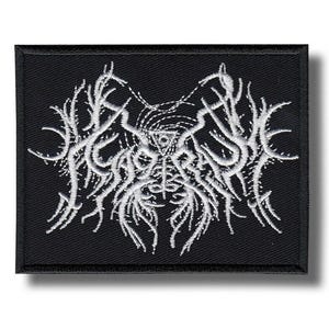 May include: A black, rectangular patch with a white, embroidered, abstract design. The design features a central element with radiating lines and organic shapes. The patch has a black border and is likely for clothing or accessories, such as a jacket or bag.