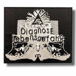 Può includere: Toppa ricamata nera con le parole "Diagnose Lebensgefahr" in filo d'argento. Il disegno comprende un occhio all'interno di un triangolo, un cervello stilizzato e due figure di animali. La toppa è rettangolare.