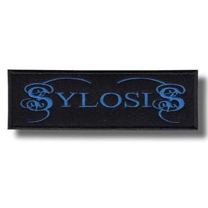 Pode incluir: Um patch retangular preto com a palavra "SYLOSIS" bordada em azul, com floreios decorativos estilizados acima e abaixo do texto. O patch é provavelmente para roupas ou acessórios.