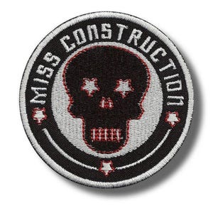 Op de afbeelding: Ronde, zwart-witte geborduurde patch met de tekst "MISS CONSTRUCTION". Een zwarte schedel met stervormige ogen en rode accenten staat in het midden. De patch heeft een witte rand en rode steraccenten.