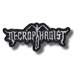 Puede incluir: Un parche bordado en blanco y negro con la palabra "NECROPHAGIST" en una fuente gótica. El parche tiene una figura estilizada en el centro. El parche es rectangular con bordes curvos.