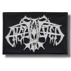 May include: Black rectangular patch with white, stylized text. The text appears to be a band logo or emblem, featuring sharp, angular lines and a gothic aesthetic. The patch is likely for clothing or accessories.
