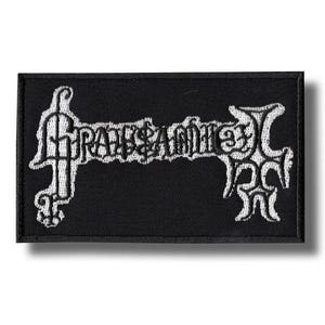 Può includere: Toppa rettangolare nera con testo ricamato bianco ed elementi decorativi. Il testo sembra essere il nome o il logo di una band. La toppa è probabilmente per abbigliamento o accessori.