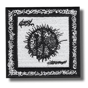 Puede incluir: Parche bordado cuadrado en blanco y negro. El parche presenta un diseño central negro y puntiagudo sobre un fondo blanco, con texto negro adicional y un borde decorativo. El parche es probablemente para ropa o accesorios.