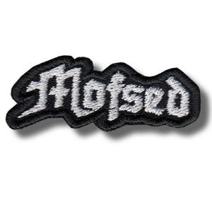 Peut inclure: Écusson brodé avec le mot "Mofsed" en blanc, avec une bordure noire. La police est stylisée. L'écusson est conçu pour être cousu sur des vêtements ou des accessoires.