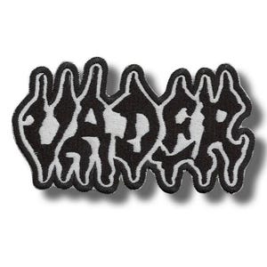 Puede incluir: Parche bordado en blanco y negro con la palabra "VADER" en una fuente estilizada y goteante. El parche tiene un fondo blanco con letras negras y un borde negro. El parche es de forma rectangular.