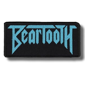 May include: A black rectangular patch featuring the word "Beartooth" in light blue, gothic-style lettering. The patch has a black border and is designed to be sewn or ironed onto clothing or accessories.