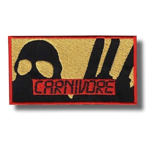 May include: Embroidered patch with a black silhouette of a gas mask and vertical lines on a gold background. The word "CARNIVORE" is in red block letters. The patch has a red border.