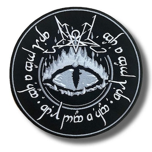Op de afbeelding: Een ronde, zwarte patch met een wit geborduurd ontwerp. Het ontwerp toont een centraal oogmotief omgeven door vlammen, een pentagram en gestileerde tekst. De patch heeft een schaduweffect.