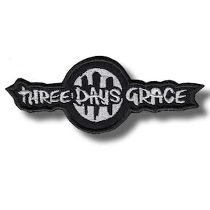 Op de afbeelding: Zwart en wit geborduurde patch met de bandnaam "THREE DAYS GRACE". De patch heeft een cirkelvormig embleem met verticale lijnen en de naam van de band in een gestileerd lettertype. De patch is rechthoekig met puntige uiteinden.