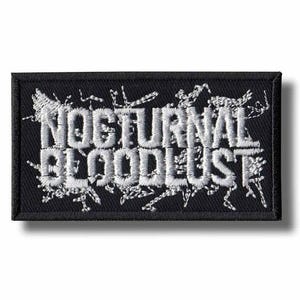 Op de afbeelding: Zwart rechthoekig embleem met de geborduurde tekst "NOCTURNAL BLOODLUST" in wit. De tekst is gestileerd met een gotisch lettertype en omgeven door witte decoratieve elementen. Het embleem heeft een zwarte rand.