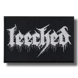 Op de afbeelding: Zwart rechthoekig embleem met het woord "Leeched" geborduurd in witte gotische letters. De letters hebben een druipend effect, wat een grunge-esthetiek toevoegt. Het embleem is waarschijnlijk bedoeld voor kleding of accessoires.