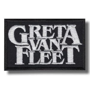 May include: A black rectangular patch featuring the embroidered words "GRETA VAN FLEET" in white. The text is arranged in three lines. The patch has a black border and is likely designed to be sewn onto clothing or bags.